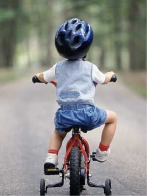 Un niño de 2 años aprende a andar en bicicleta de equilibrio en la  carretera de la aldea en la primavera